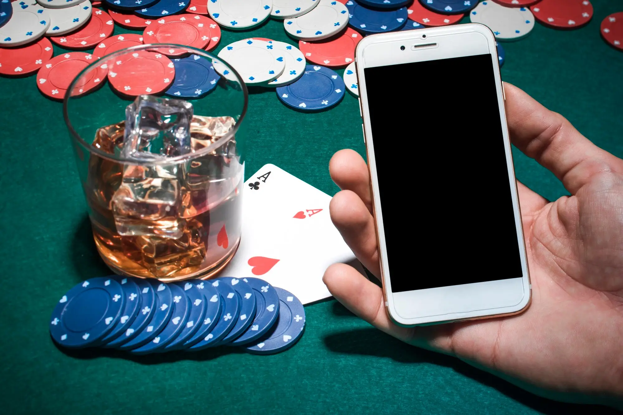 Mobiltelefon ved pokerbord med sjetonger, kort og whisky